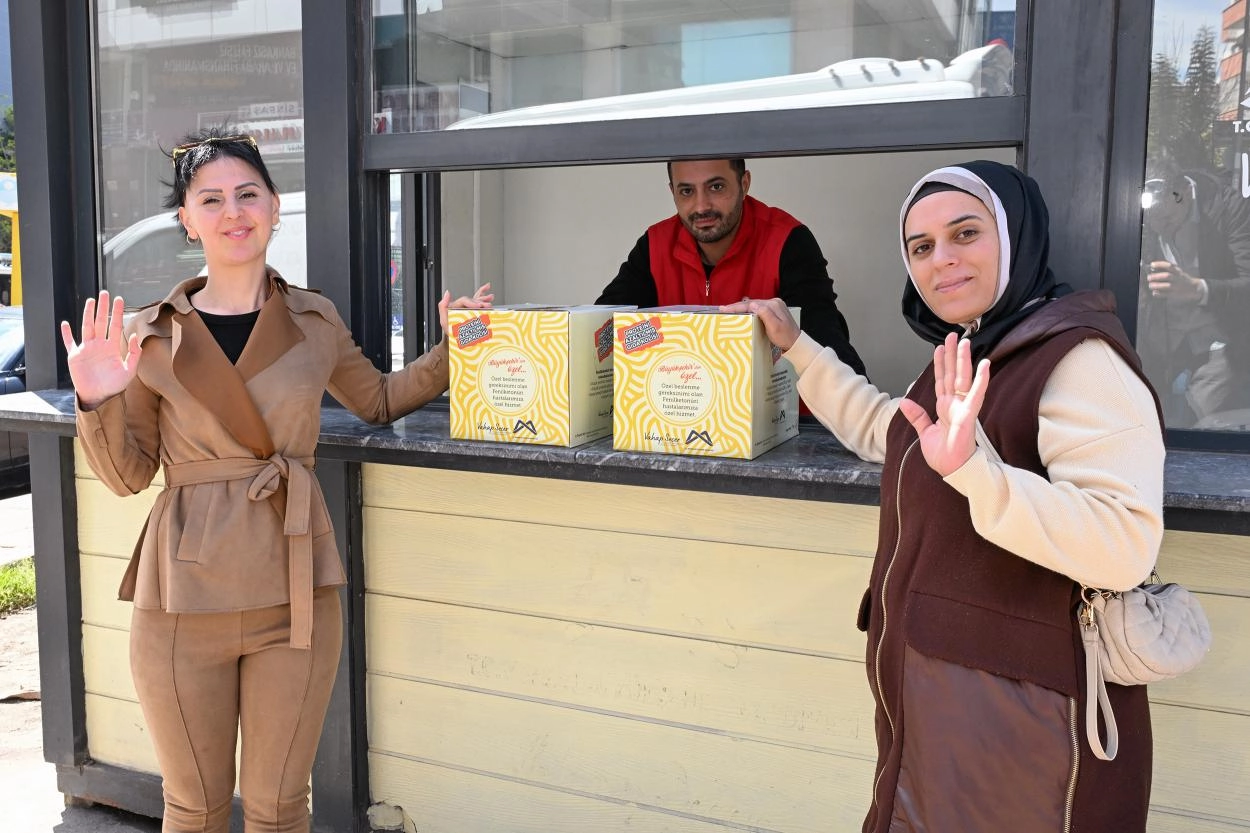 Mersin Büyükşehir Belediyesi'nin fenilketonüri hastalarına özel gıda kolisi dağıttığı anı gösteren görsel.